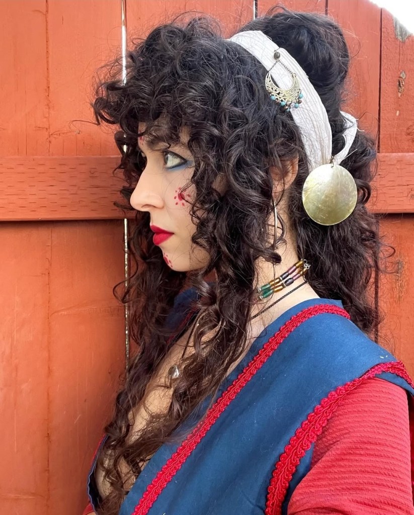 an impressive example of a Minoan/Mycenaean-inspired look by Greek cosplayer Persephonaae. She is waring a blue and red bodice and has long curly black hair